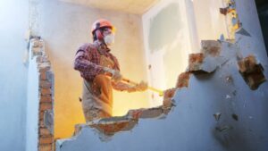 worker with sledgehammer at indoor wall destroying